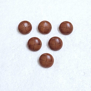 May include: Six brown leather buttons with a woven pattern. The buttons are arranged in a triangle shape.