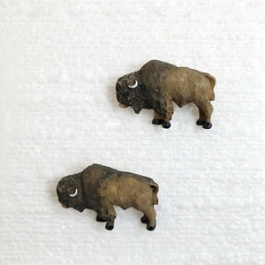 Peut inclure: Deux figurines de bisons brunes et noires. Les bisons sont debout sur une surface blanche.