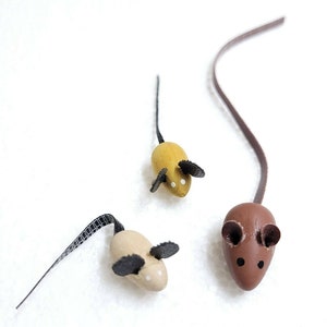 May include: Three wooden toy mice with black felt ears and tails. The mice are brown, yellow, and beige.