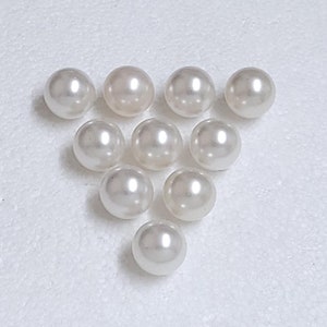 May include: A group of ten white round pearls, arranged in a triangular shape on a white surface.