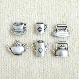 Puede incluir: Un conjunto de seis dijes de metal en tono plateado con forma de artículos domésticos en miniatura, que incluyen una taza de té sobre un platillo, una taza con un emblema de estrella, una plancha, una tetera, una cafetera alta y una tetera.