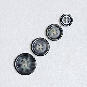 May include: Four black and white mottled buttons with four holes each, arranged in a line from largest to smallest.