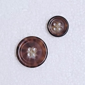 May include: Two brown and white patterned buttons with four holes each. The larger button is about 1.5 inches in diameter and the smaller button is about 1 inch in diameter.