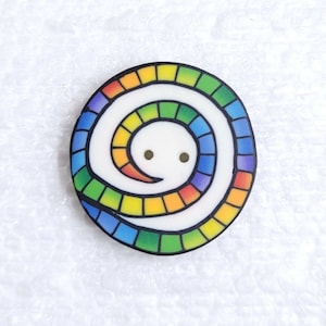 May include: A round button with a white background and a rainbow spiral design. The spiral is made up of small squares of different colors, including red, orange, yellow, green, blue, indigo, and violet.