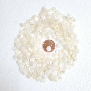 May include: A large pile of white, round, mother-of-pearl buttons. The buttons are arranged in a circle around a copper-colored coin.