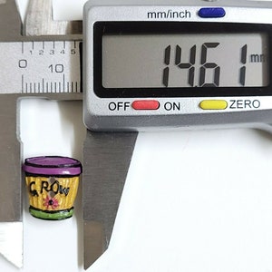 May include: A small, yellow ceramic planter with a purple rim and the word "GROW" written on it. The planter is 1.46 inches in diameter.