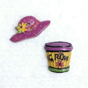 Op de afbeelding: Twee kleurrijke knopen, een in de vorm van een paarse hoed met een gele bloem en de andere in de vorm van een gele bloempot met het woord "GROW" erop.