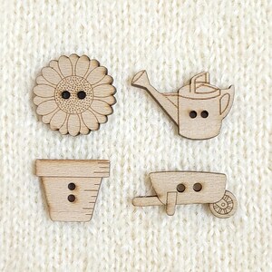 Peut inclure: Quatre boutons en bois clair en forme d'objets de jardin. Un bouton représente un tournesol, un autre un arrosoir, un troisième un pot de fleurs et le dernier une brouette. Chaque bouton possède deux petits trous pour la couture.