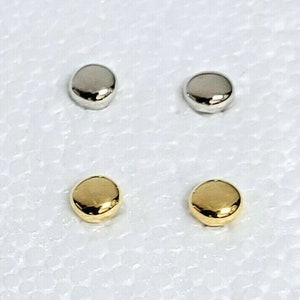 Könnte beinhalten: Zwei Paare kleiner, runder, flacher Ohrringe. Ein Paar ist silberfarben und das andere Paar ist golden.