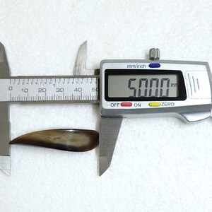 May include: A brown, curved object is measured with a digital caliper. The caliper displays a measurement of 5.000 mm. The object has a smooth, polished appearance with variations in color.
