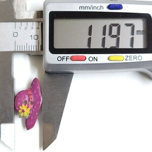 May include: A close-up of a purple and yellow button shaped like a hat with a flower design. The button is being measured with a caliper, which reads 1.97 mm.