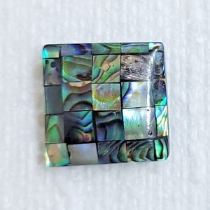 May include: A square-shaped mosaic tile made of iridescent abalone shell. The tile has a green, blue, and purple color scheme.