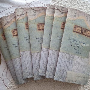 Może przedstawiać: Stos papierowych broszur w stylu vintage o postarzanym, postarzałym wyglądzie. Każda broszura ma jasnoniebieską i beżową kolorystykę, z nadrukowanym tekstem, znaczkami pocztowymi i ręcznym pismem. Broszury są związane cienkimi, ciemnymi nićmi.
