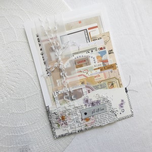 K&ouml;nnte beinhalten: Ein wei&szlig;er Umschlag mit einem gen&auml;hten Rand, gef&uuml;llt mit Vintage-Ephemera, darunter Papierschnipsel, Briefmarken und ein kleines Etikett mit der Aufschrift "Mit Liebe f&uuml;llen".