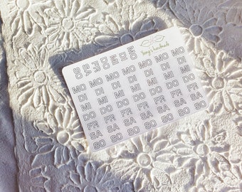 May include: A sheet of white stickers with black outlines of the days of the week. The stickers are arranged in rows and columns, with each sticker containing a single day of the week. The stickers are labeled "SO", "SA", "FR", "DO", "MO", "DI", "MI", and "SO".