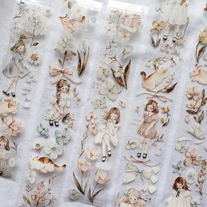 Peut inclure: Ruban adh&eacute;sif d&eacute;coratif avec des illustrations &agrave; l'aquarelle de filles, de fleurs, de chats et de lapins aux couleurs pastel douces. Le ruban a un fond transparent et comprend des accents floraux et des n&oelig;uds, cr&eacute;ant une esth&eacute;tique fantaisiste et vintage.