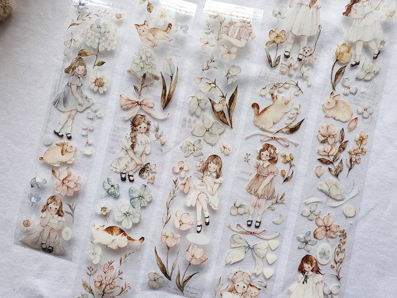 Peut inclure: Ruban adh&eacute;sif d&eacute;coratif avec des illustrations &agrave; l'aquarelle de filles, de fleurs, de chats et de lapins aux couleurs pastel douces. Le ruban a un fond transparent et comprend des accents floraux et des n&oelig;uds, cr&eacute;ant une esth&eacute;tique fantaisiste et vintage.