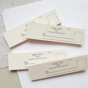 Könnte beinhalten: Ein Stapel cremefarbener Buchpostkarten mit schwarzem Text, der "Book Post Card" und "Wiesbaden Stadtbibliothek" und "No." und "To." lautet.