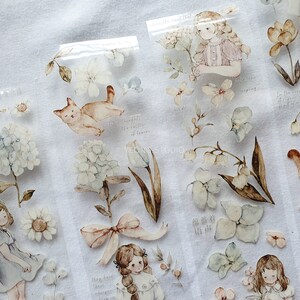 Peut inclure: Autocollants aquarelle avec des illustrations de filles, de fleurs et d'un chat. Les autocollants ont une palette de couleurs pastel douces avec des d&eacute;tails comme des n&oelig;uds, des hortensias et des tulipes. Certains autocollants ont du texte manuscrit.