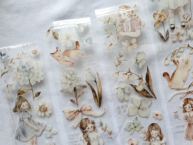 Peut inclure: Autocollants aquarelle avec des illustrations de filles, de fleurs et d'un chat. Les autocollants ont une palette de couleurs pastel douces avec des d&eacute;tails comme des n&oelig;uds, des hortensias et des tulipes. Certains autocollants ont du texte manuscrit.