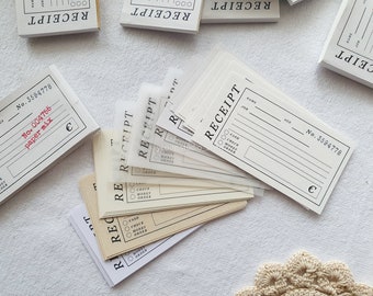 May include: A stack of white receipt paper pads with the word "RECEIPT" printed on the front. The pads are in various sizes and have different numbers printed on them. The pads are on a white surface.