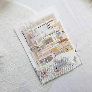 K&ouml;nnte beinhalten: Ein wei&szlig;er Umschlag mit einem gen&auml;hten Rand, gef&uuml;llt mit Papier-Ephemera im Vintage-Stil, darunter Dekorpapier, Aufkleber und ein Etikett mit der Aufschrift "Mit Liebe f&uuml;llen".
