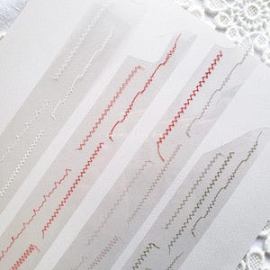 May include: Five samples of different sewing machine stitch patterns on clear plastic sheets. The stitches are white, red, grey, and green.