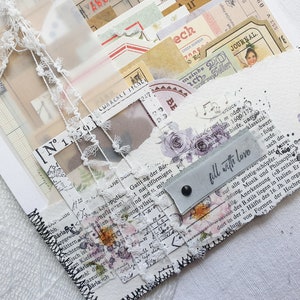 K&ouml;nnte beinhalten: Ein wei&szlig;es Papierjournal mit einem schwarzen, gesteppten Rand. Das Journal ist mit Spitze, Papierschnipseln und einem Etikett verziert, auf dem "f&uuml;lle mit Liebe" steht.