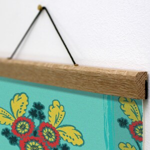 May include: A floral art print with a wooden hanger. The print features red and yellow flowers on a teal background. The wooden hanger is light brown and is suspended by a black cord.