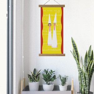 May include: A vertical wall hanging with a yellow background featuring musical notes and the text "Hark, the Herald Angels Sing." Two figures in white robes and tall hats are depicted. The artwork is framed with wooden bars.