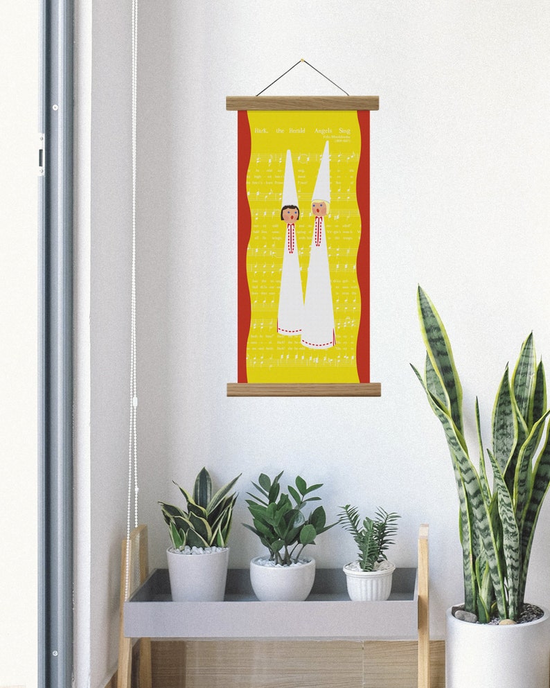 May include: A vertical wall hanging with a yellow background featuring musical notes and the text "Hark, the Herald Angels Sing." Two figures in white robes and tall hats are depicted. The artwork is framed with wooden bars.