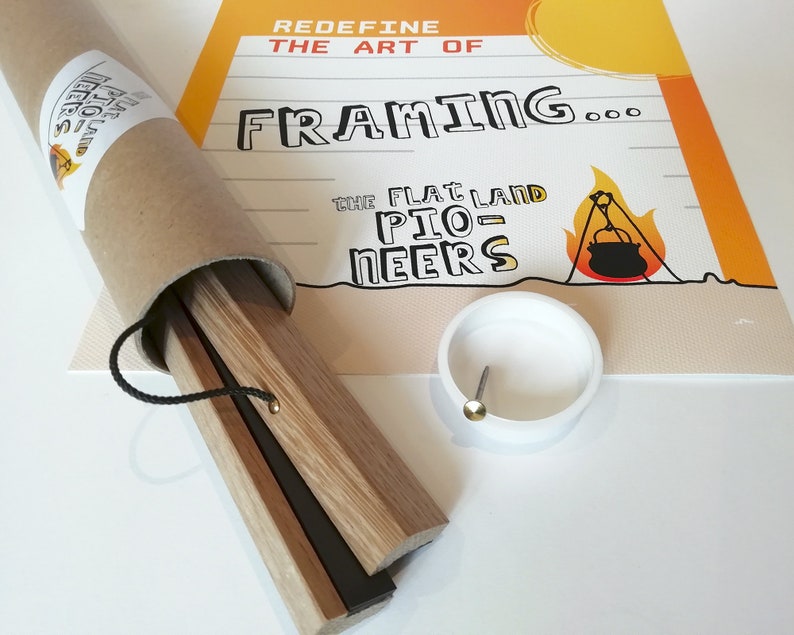 K&ouml;nnte beinhalten: Ein Poster-Rahmen-Set mit Holzleisten, einer schwarzen Kordel und einem wei&szlig;en Kunststoffteil mit einem Metallstift. Das Set ist in einer braunen Pappr&ouml;hre verpackt. Das Poster im Hintergrund tr&auml;gt den Text "Redefine the Art of Framing..." und eine Campingszene.