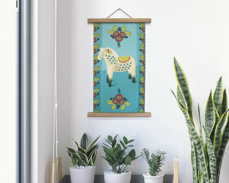 K&ouml;nnte beinhalten: Ein gerahmter Wandkunstdruck mit einem stilisierten wei&szlig;en Pferd mit gelbem Sattel und gr&uuml;nen Punkten auf t&uuml;rkisfarbenem Hintergrund. Der Druck ist mit floralen Mustern in Rot, Gelb und Gr&uuml;n verziert und wird mit einem Holzrahmen pr&auml;sentiert.