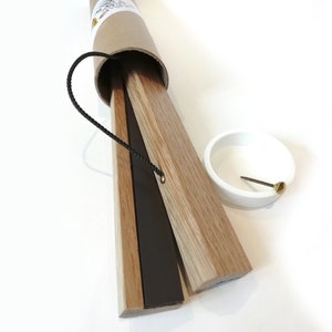 K&ouml;nnte beinhalten: Ein Satz magnetischer Posteraufh&auml;nger aus Holz in einer braunen Papprolle. Die Aufh&auml;nger sind hellbraun mit einem schwarzen Magnetstreifen. Eine kleine wei&szlig;e Schale und eine Messingstiftspitze sind ebenfalls vorhanden.