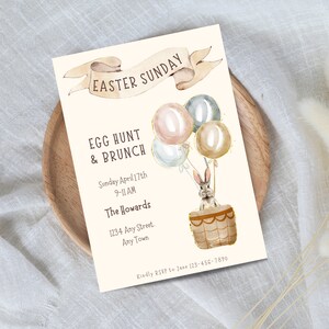 May include: An invitation to an Easter Sunday egg hunt and brunch. The invitation features a watercolor illustration of a bunny in a hot air balloon with pastel colored balloons. The text reads "Easter Sunday", "Egg Hunt & Brunch", "Sunday April 17th 9-11 AM", "The Howards", "1234 Any Street. Any Town", and "Kindly RSVP to Jane 123-456-7890".