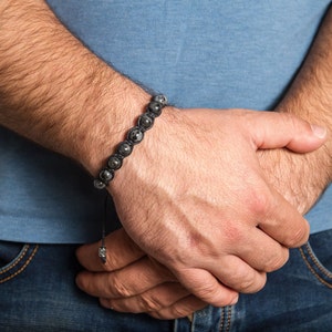 May include: A black beaded bracelet with silver accents on a person's wrist.