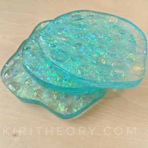 May include: Three iridescent blue glass coasters with a textured surface. The coasters are stacked on top of each other.