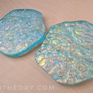 May include: Two iridescent blue glass coasters with a textured surface. The coasters are shaped like irregular circles.