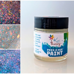 May include: A small jar of iridescent white paint with the text "Kivi theory" and "PEEK A HUE PAINT" on the label. The paint is multi-hued acrylic paint for daring artists who like to experiment.