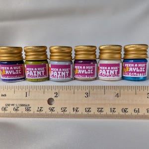 A wood ruler showing six colorful petite glass jars lined up above it for scale. The six jars are lined up straight with no spaces between, and they add up to about 5 inches total when they line up together in the image. Each jar is 1.25 inches tall.