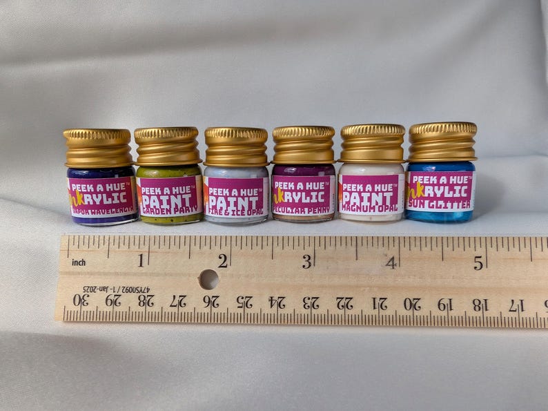 A wood ruler showing six colorful petite glass jars lined up above it for scale. The six jars are lined up straight with no spaces between, and they add up to about 5 inches total when they line up together in the image. Each jar is 1.25 inches tall.