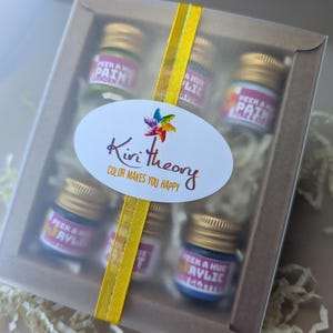 a colorful festive slide out box of petite acrylic ink and paint samples jars, with a bright yellow ribbon and cute colorful label.