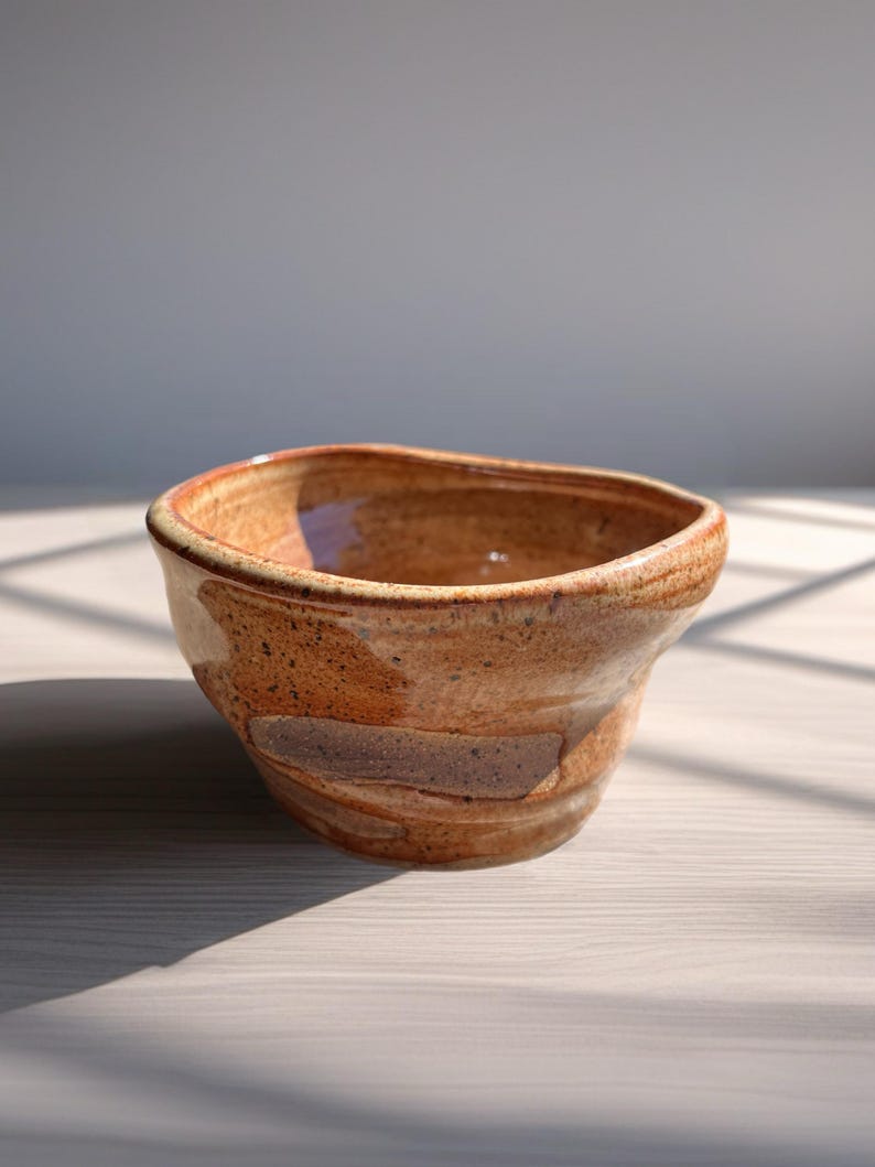 Peut inclure: Un bol en c&eacute;ramique fait &agrave; la main avec un design rustique et organique. Le bol pr&eacute;sente une palette de couleurs chaudes et terreuses avec des nuances de brun et de beige. Le bord a une forme l&eacute;g&egrave;rement irr&eacute;guli&egrave;re, ajoutant &agrave; son attrait artisanal unique.