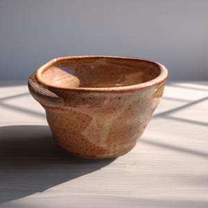 Peut inclure: Une tasse en c&eacute;ramique blanche avec une anse noire et le texte "But First, Coffee" en gras noir. La tasse est pos&eacute;e sur un fond neutre, soulignant son design simple.