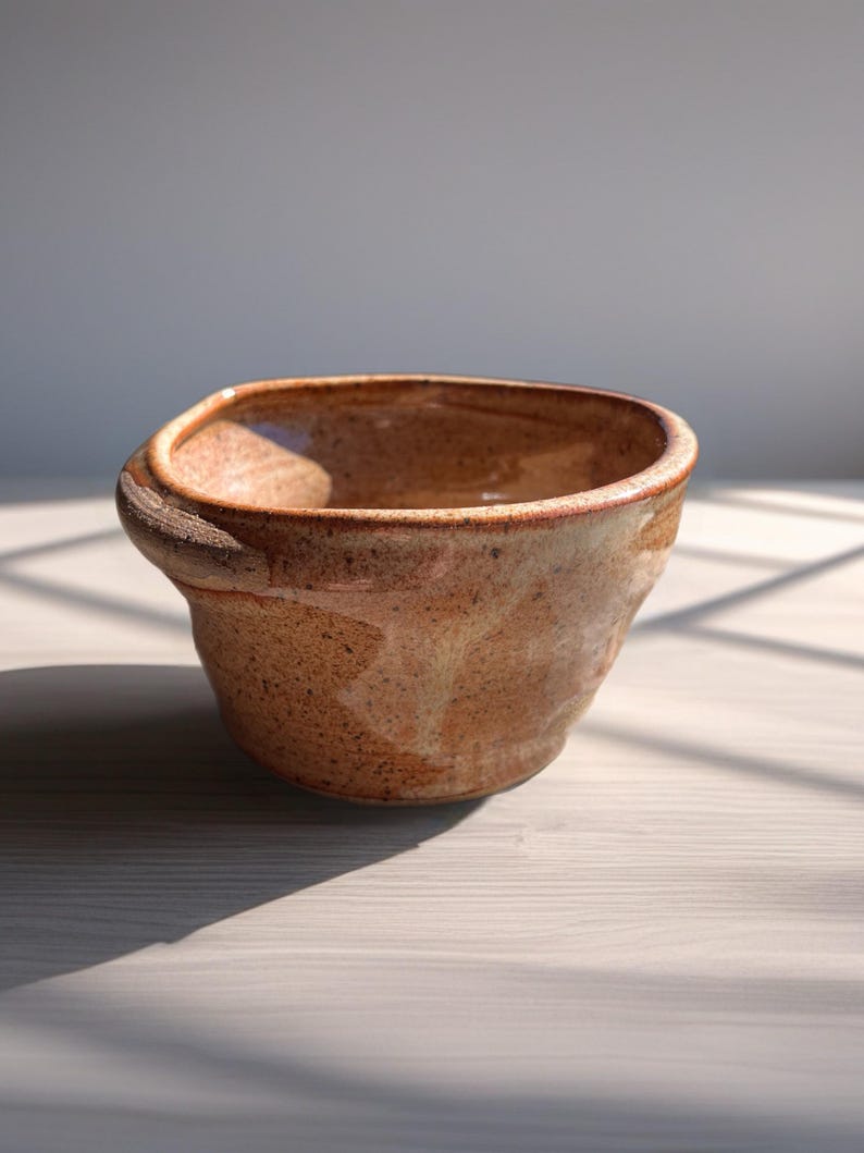 Peut inclure: Une tasse en c&eacute;ramique blanche avec une anse noire et le texte "But First, Coffee" en gras noir. La tasse est pos&eacute;e sur un fond neutre, soulignant son design simple.