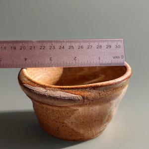 Peut inclure: Un petit bol en c&eacute;ramique fait &agrave; la main avec une esth&eacute;tique rustique et terreuse. Le bol est de couleur marron chaud avec des accents marron plus fonc&eacute;s autour du bord. Le bol mesure environ 7.6 cm de diam&egrave;tre.