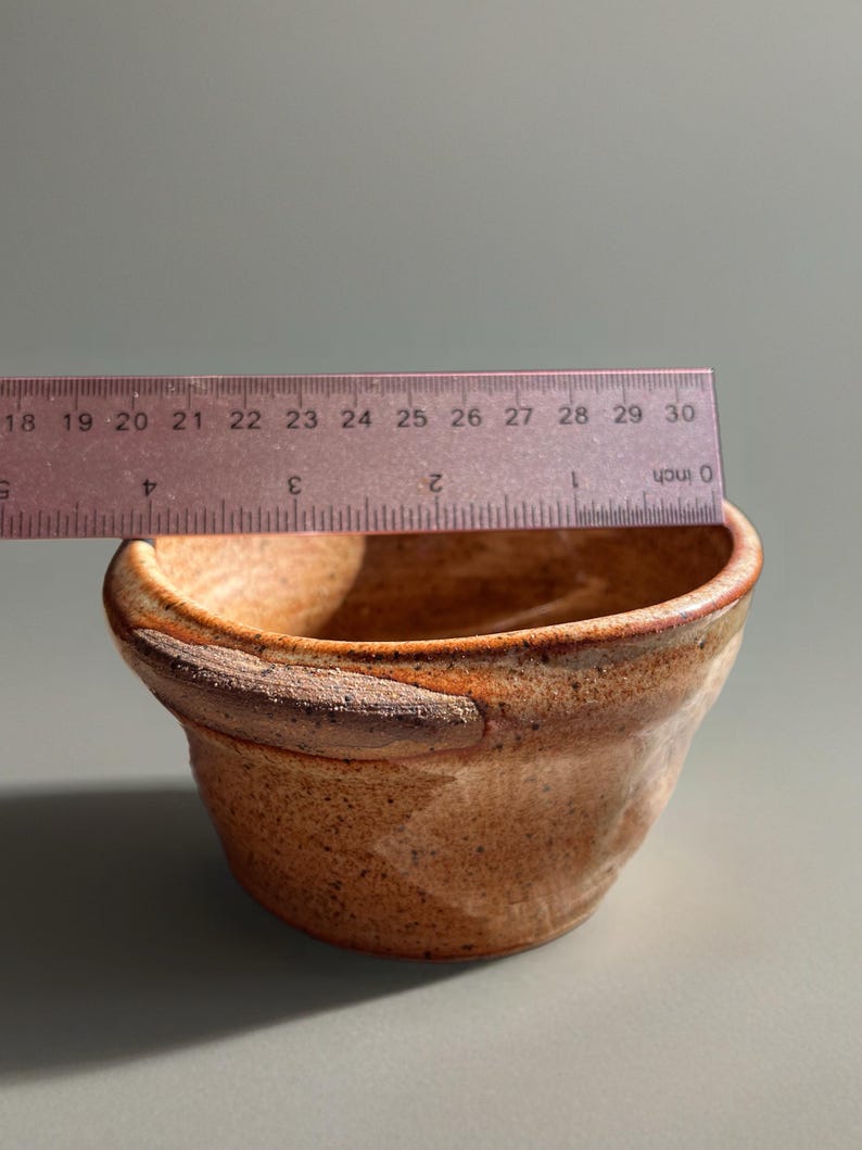 Peut inclure: Un petit bol en c&eacute;ramique fait &agrave; la main avec une esth&eacute;tique rustique et terreuse. Le bol est de couleur marron chaud avec des accents marron plus fonc&eacute;s autour du bord. Le bol mesure environ 7.6 cm de diam&egrave;tre.