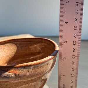 Peut inclure: Un bol en c&eacute;ramique fait &agrave; la main avec un gla&ccedil;age marron tachet&eacute; et un bord marron fonc&eacute;. Le bol mesure environ 7.6 cm de hauteur, mesur&eacute; avec une r&egrave;gle. Le bol repose sur une surface de couleur claire.