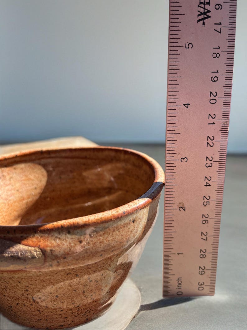 Peut inclure: Un bol en c&eacute;ramique fait &agrave; la main avec un gla&ccedil;age marron tachet&eacute; et un bord marron fonc&eacute;. Le bol mesure environ 7.6 cm de hauteur, mesur&eacute; avec une r&egrave;gle. Le bol repose sur une surface de couleur claire.