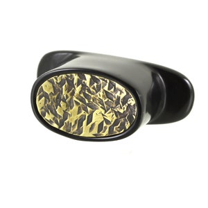 May include: Black and gold oval-shaped bottle stopper with a geometric pattern.